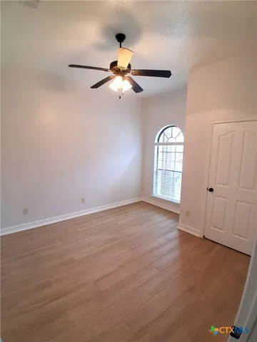 an empty room with wooden floor fan and windows