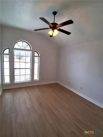 an empty room with wooden floor fan and windows