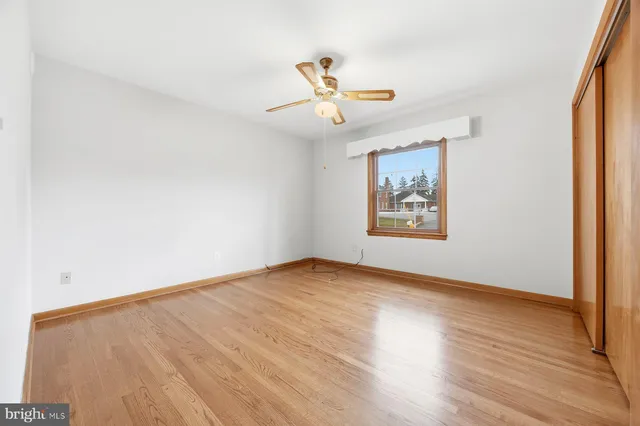 an empty room with wooden floor ceiling fan and windows