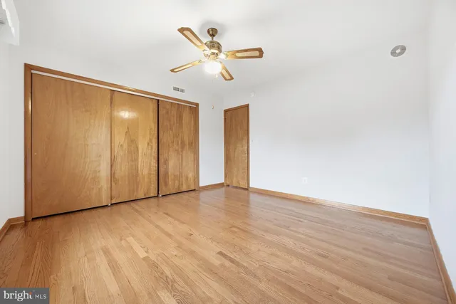 a view of an empty room with wooden floor and a ceiling fan