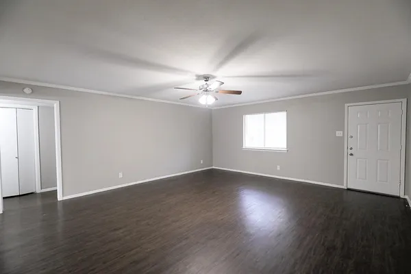 an empty room with wooden floor chandelier fan and windows