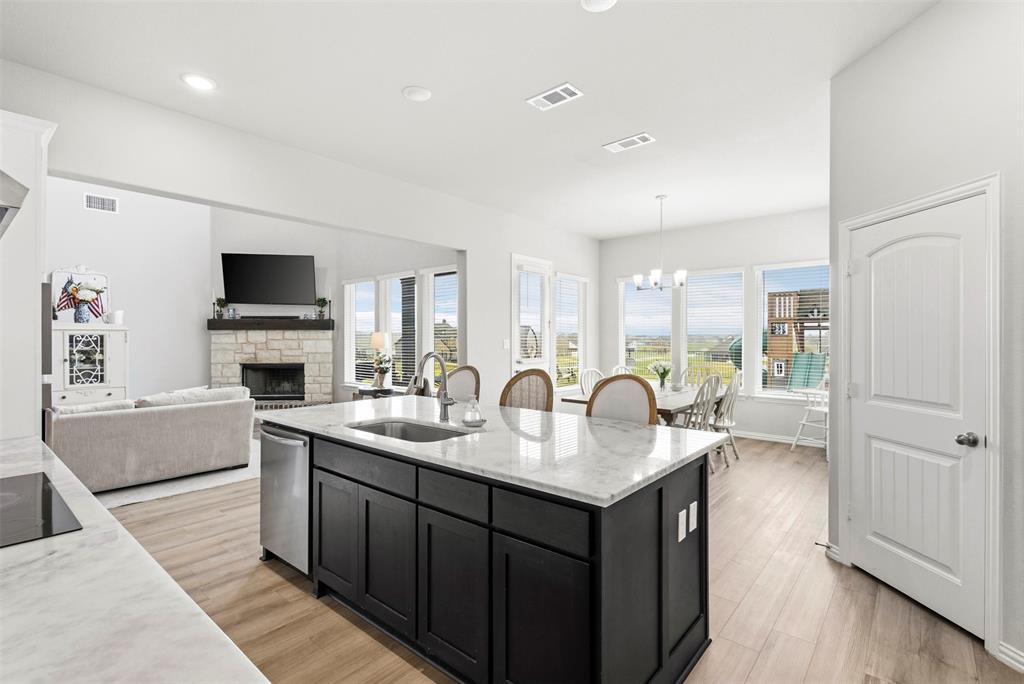 107 Yampa Court Rhome, TX 76078 - Photo 2 of 30 Open-concept living space featuring a central kitchen island with a built-in sink and dishwasher, light wood-finish flooring, and expansive windows