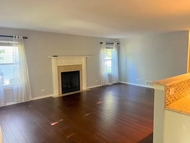 an empty room with wooden floor fireplace and windows