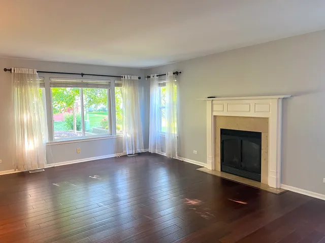 an empty room with wooden floor fireplace and windows