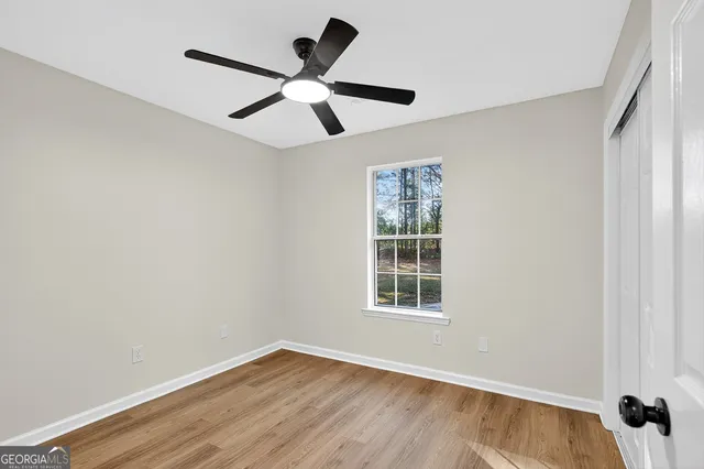 an empty room with wooden floor ceiling fan and windows