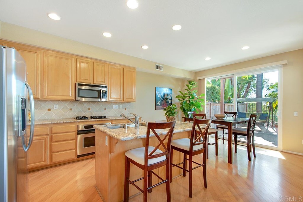 1723 Bluebird Lane Carlsbad, CA 92011 - Photo 10 of 33 a kitchen with stainless steel appliances granite countertop wooden floor dining table and chairs