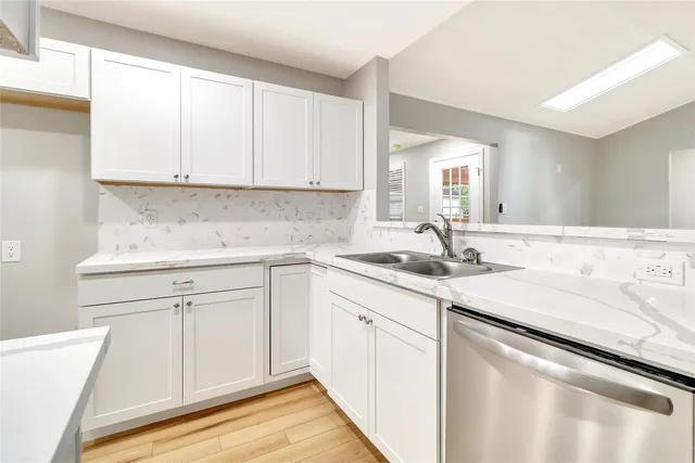 a kitchen with a sink dishwasher and white cabinets with wooden floor