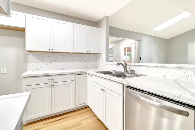 a kitchen with a sink dishwasher and white cabinets with wooden floor