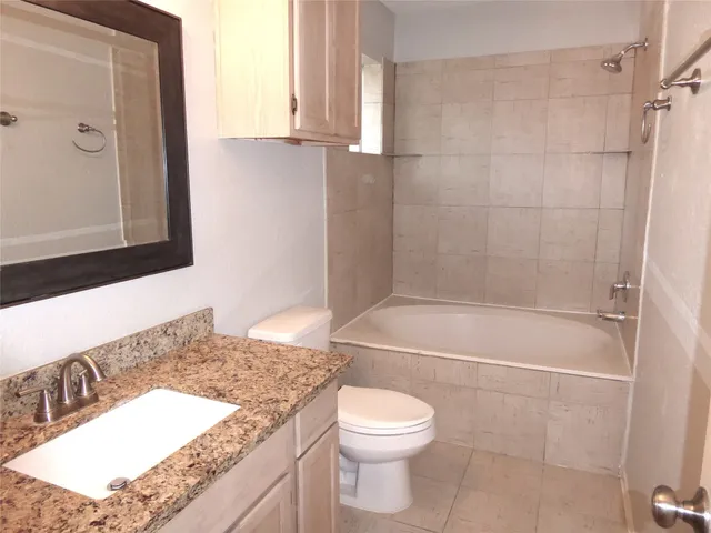 a bathroom with a granite countertop bathtub sink vanity mirror and toilet