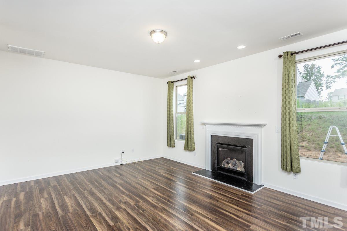 1417 Lombar Street Raleigh, NC 27610 - Photo 6 of 19 an empty room with wooden floor a fireplace and windows
