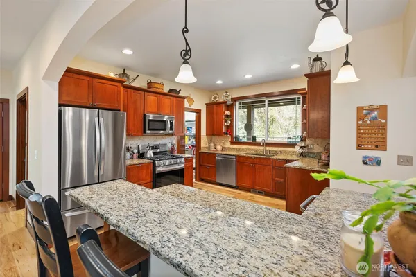 a kitchen with stainless steel appliances kitchen island granite countertop a table chairs and a wooden floor