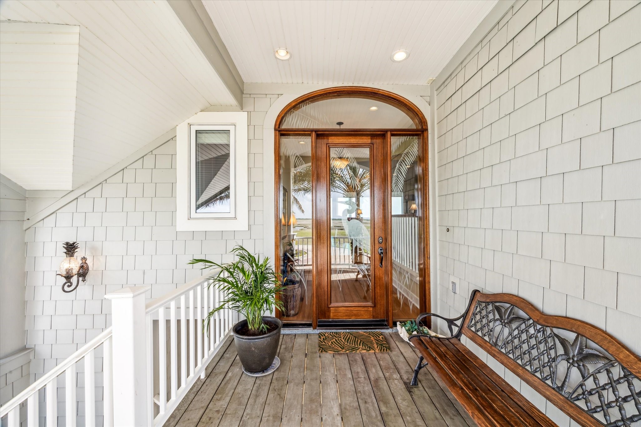 1 Shell Key Hitchcock, TX 77563 - Photo 7 of 50 Welcome guests in style with this inviting front entry, featuring rich wood-framed etched glass door beneath an elegant arched transom. The covered porch is accented with low-maintenance Hardie shingle siding, warm-toned IPE decking, and coastal-inspired details including a decorative wall sconce and classic white railing, making this space the perfect transition into the relaxed yet refined interior of the home