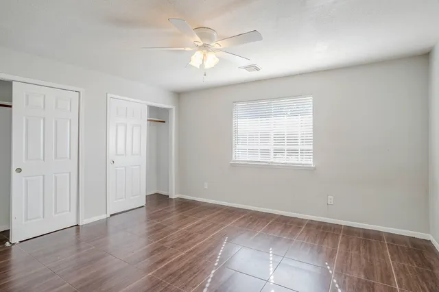 an empty room with wooden floor chandelier fan and windows