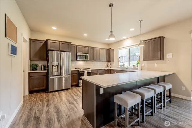 a kitchen with stainless steel appliances a dining table chairs refrigerator and wooden floor