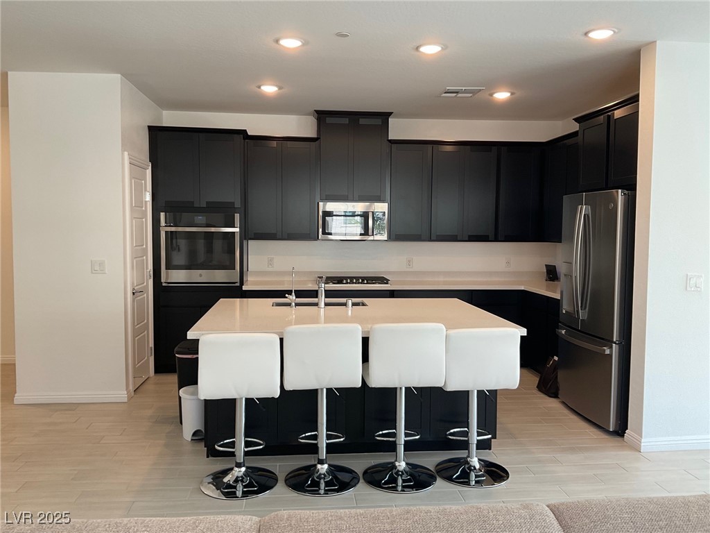 2555 Hampton Road, Unit 4209 Henderson, NV 89052 - Photo 9 of 67 Kitchen with dark cabinetry, a breakfast bar, appliances with stainless steel finishes, wood tiled floors, and an island with sink