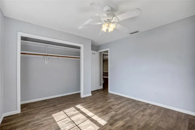 a view of an empty room with wooden floor and fan