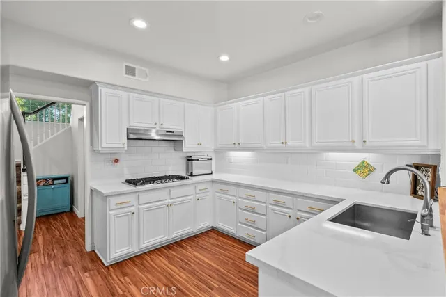 a kitchen with a sink dishwasher and white cabinets with wooden floor