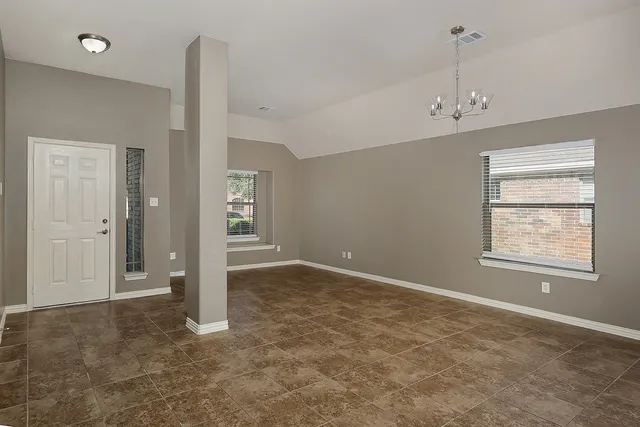 an empty room with chandelier fan and windows