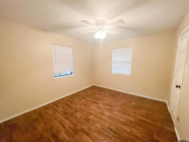 an empty room with wooden floor fan and windows