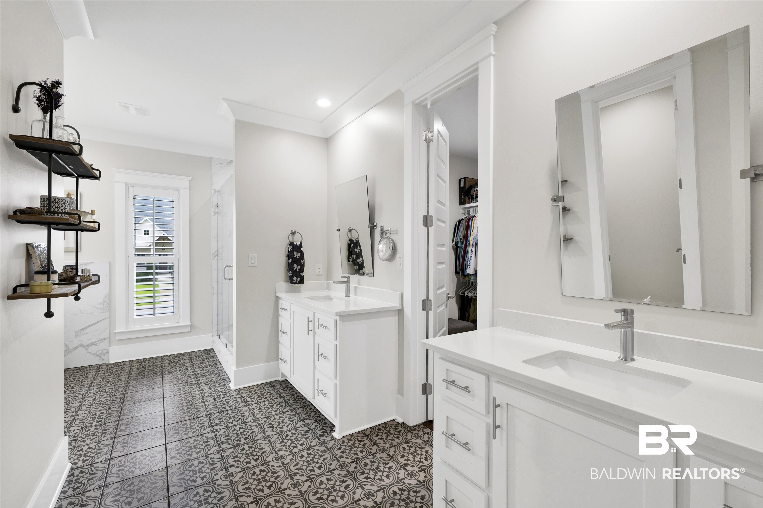 21702 Pillars Street Fairhope, AL 36532 - Photo 21 of 54 Spacious bathroom featuring patterned floor tiling, dual white vanities with integrated sinks and chrome fixtures, a glass-enclosed shower, and a window with plantation shutters