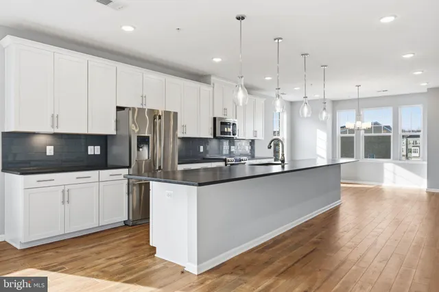 a kitchen with stainless steel appliances granite countertop a refrigerator a sink a stove a microwave and white cabinets with wooden floor