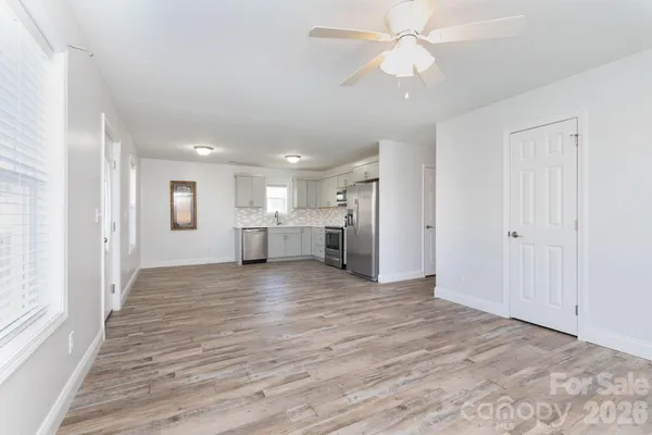 a view of an empty room with window wooden floor and a kitchen