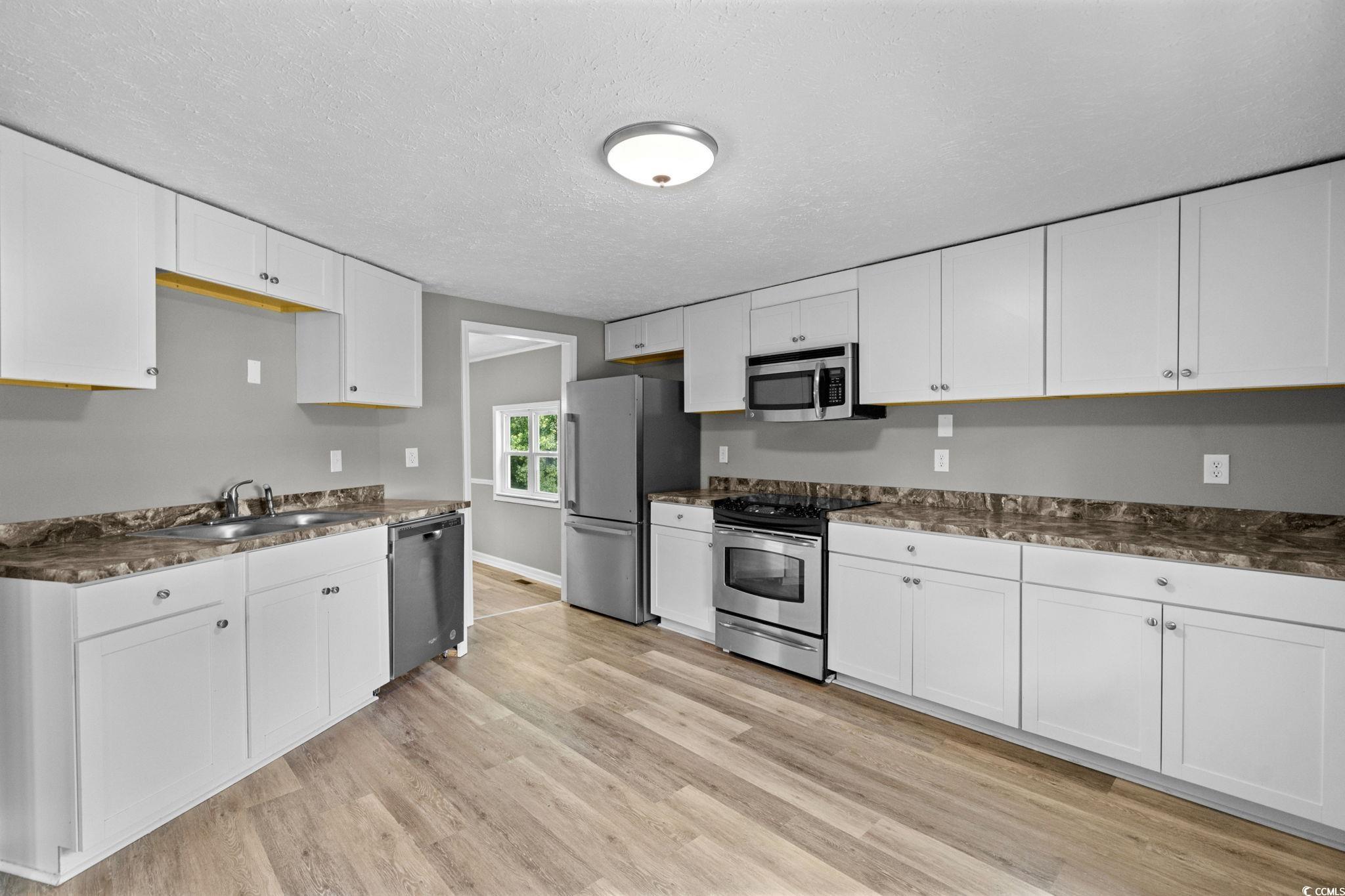 450 Highway 348 Loris, SC 29569 - Photo 14 of 37 Kitchen featuring white cabinets, stainless steel appliances, dark countertops, a textured ceiling, and light wood-style flooring