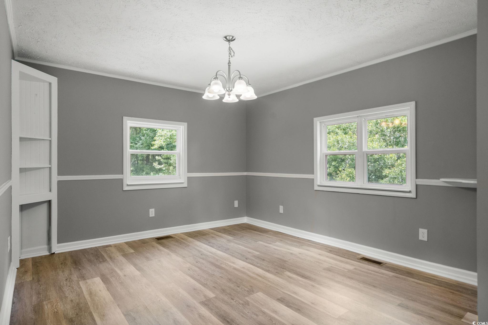 450 Highway 348 Loris, SC 29569 - Photo 10 of 37 Unfurnished dining area with healthy amount of natural light, light wood-type flooring, ornamental molding, a chandelier, and a textured ceiling