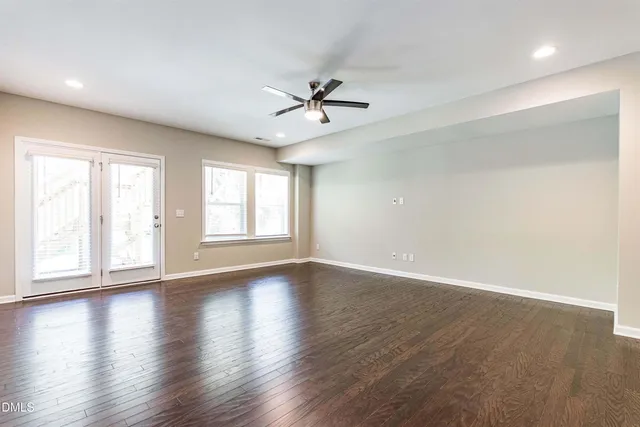 an empty room with wooden floor ceiling fan and windows