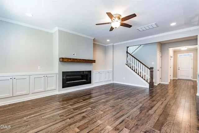 an empty room with wooden floor a ceiling fan a fireplace and windows