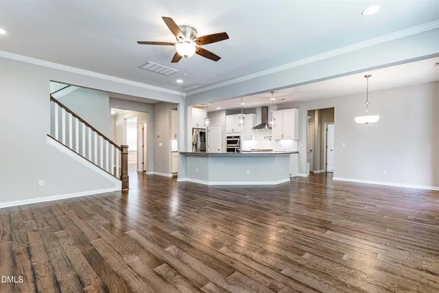 a view of an empty room and kitchen with wooden floor