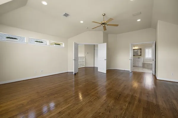 a view of an empty room with wooden floor and a ceiling fan