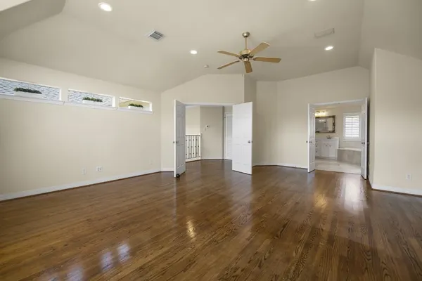 a view of an empty room with wooden floor and a ceiling fan