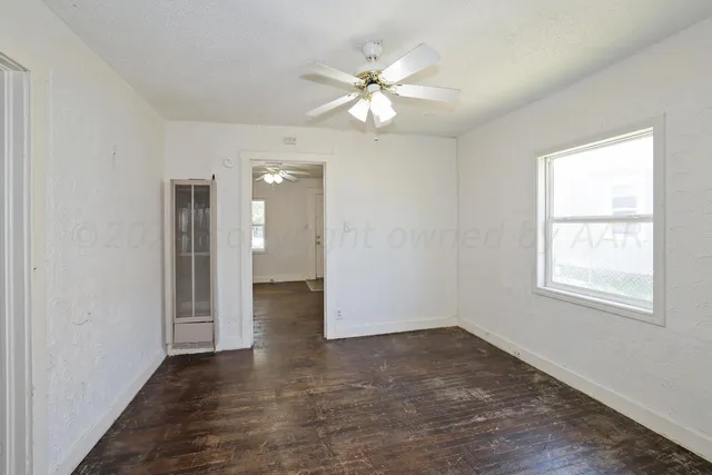 a view of an empty room with wooden floor and a window