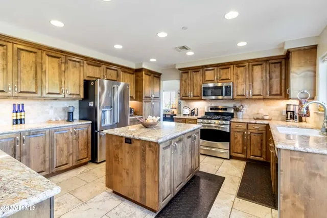 a kitchen with kitchen island granite countertop a stove top oven a refrigerator a sink and dishwasher with wooden floor