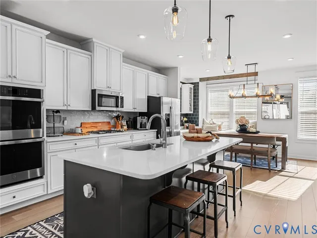 a kitchen with stainless steel appliances granite countertop a stove a refrigerator a sink a dining table and chairs with wooden floor