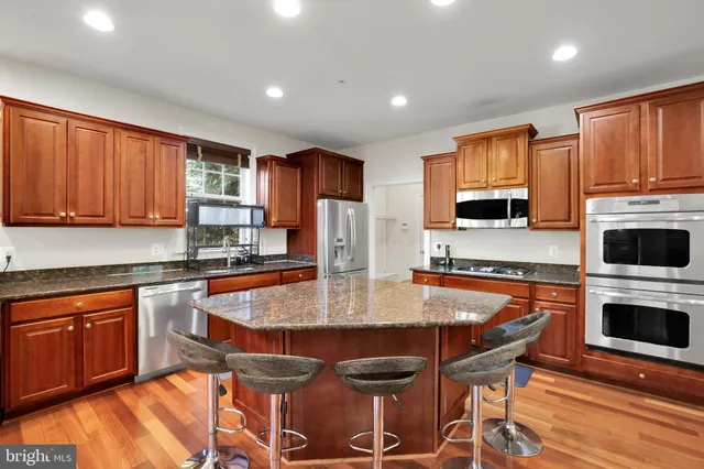 a kitchen with stainless steel appliances granite countertop a stove top oven a sink dishwasher a dining table and chairs with wooden floor