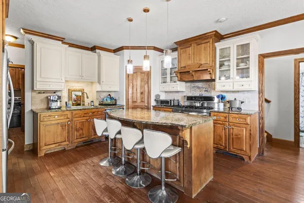 a kitchen with stainless steel appliances granite countertop a stove a sink a refrigerator and white cabinets with wooden floor