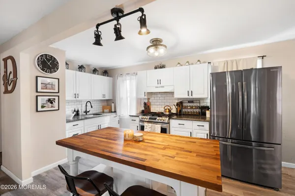 a kitchen with stainless steel appliances granite countertop a refrigerator a stove a sink dishwasher and white cabinets with wooden floor