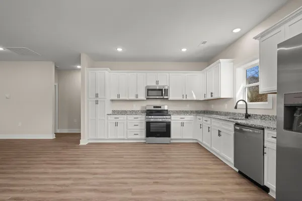 a large kitchen with stainless steel appliances granite countertop a stove top oven a sink dishwasher and a refrigerator with wooden floor
