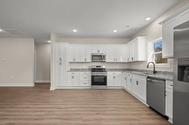 a large kitchen with stainless steel appliances granite countertop a stove top oven a sink dishwasher and a refrigerator with wooden floor