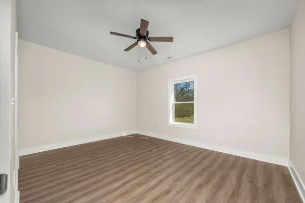 an empty room with wooden floor ceiling fan and windows