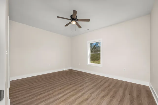 an empty room with wooden floor ceiling fan and windows