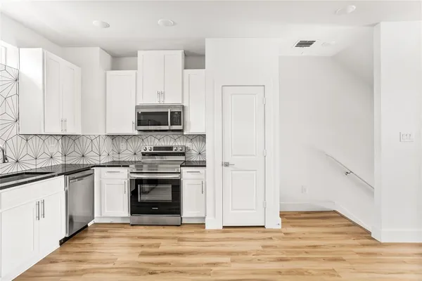 a kitchen with a refrigerator a stove top oven and white cabinets