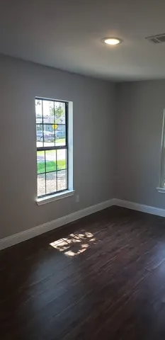 a view of an empty room with wooden floor and a window