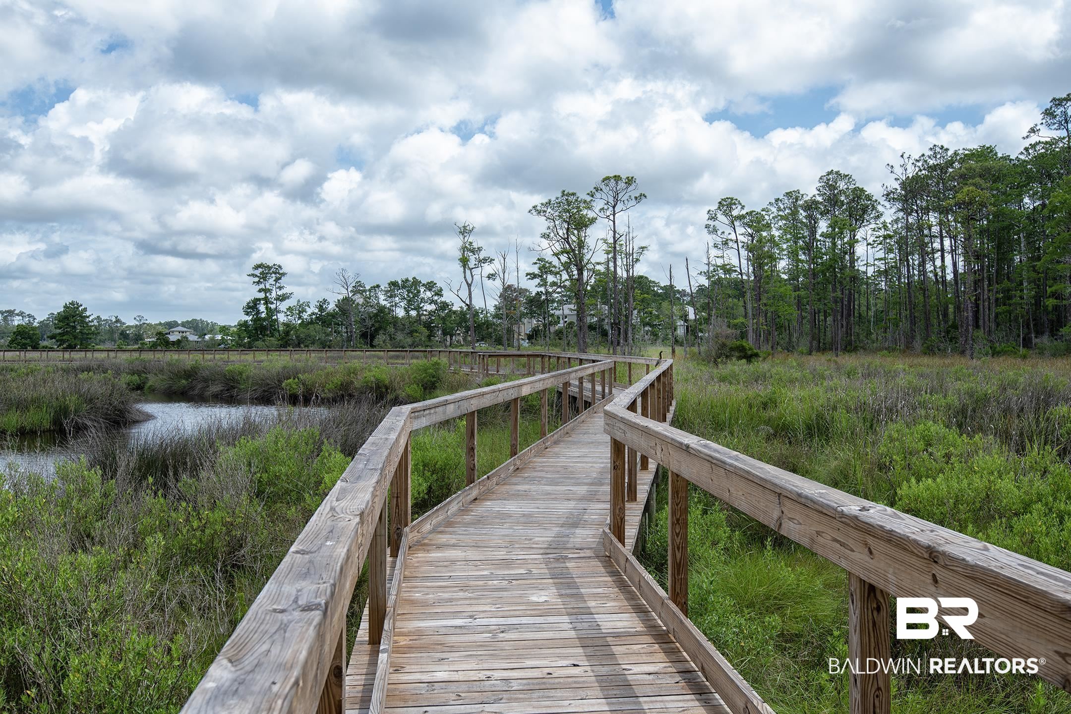 18754 Treasure Oaks Road Gulf Shores, AL 36542 - Photo 52 of 53 Wood-plank boardwalk traversing a natural wetland landscape with lush green foliage, a winding waterway, and mature trees in the background
