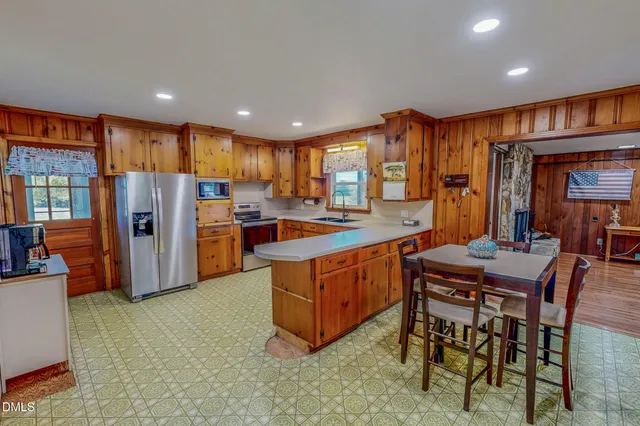 a kitchen with stainless steel appliances granite countertop a refrigerator a sink dishwasher a dining table and chairs with wooden floor