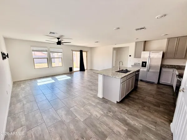 a large white kitchen with granite countertop a stove a sink a refrigerator and white cabinets with wooden floor