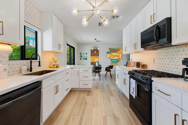 a kitchen with stainless steel appliances a stove top oven a sink dishwasher a dining table and chairs with wooden floor