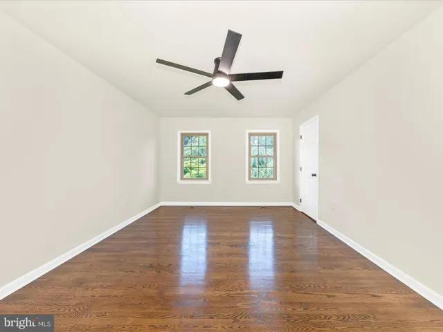 an empty room with wooden floor fan and windows